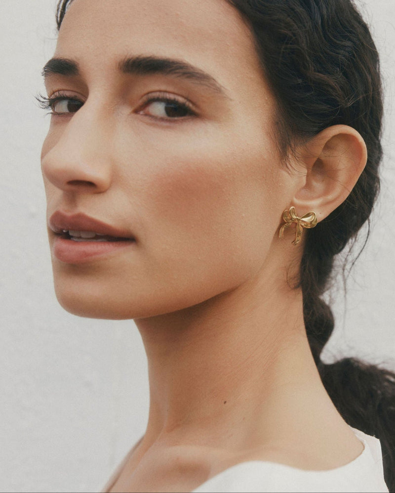 Woman with a side braid wearing gold earrings against a plain background